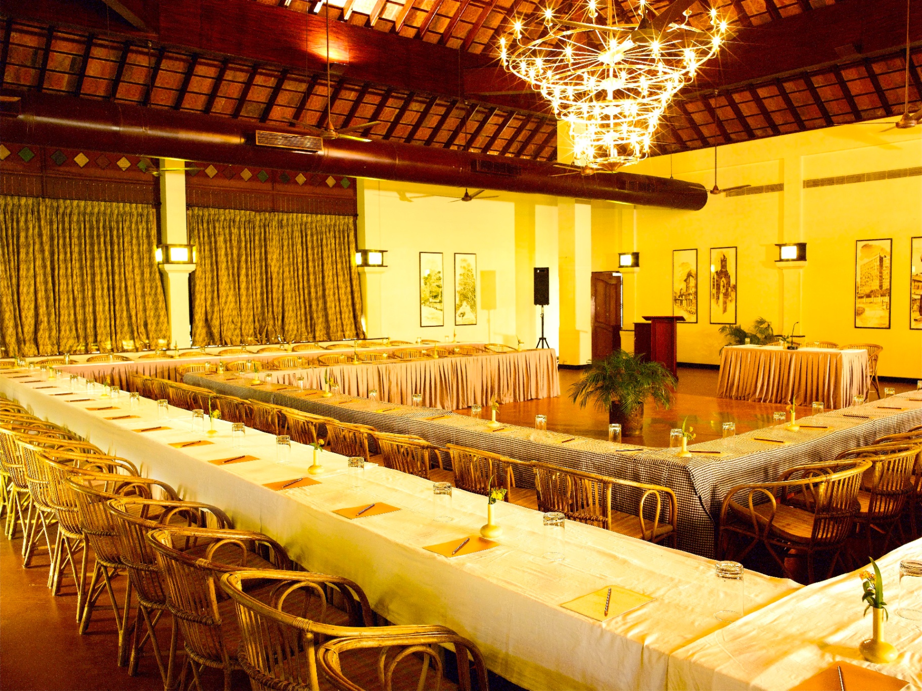 Vedhi banquet hall set with U-shaped tables beneath a timber roof and chandelier
