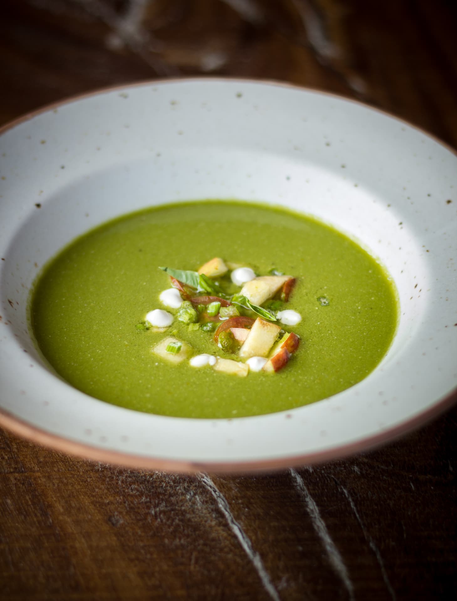 Bowl of bright green vegetable soup garnished with apple and herbs at Prakriti Shakti