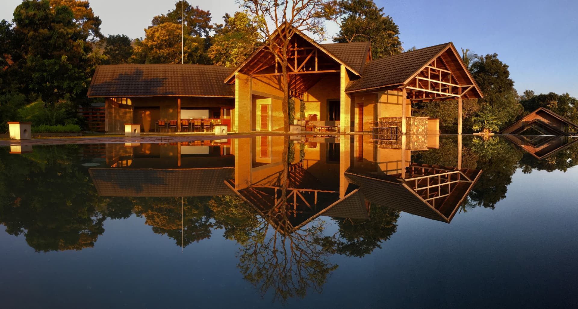Prakriti Shakti Panchalimedu Kerala CGH Earth — timber and brick pavilions reflected in still water at golden hour