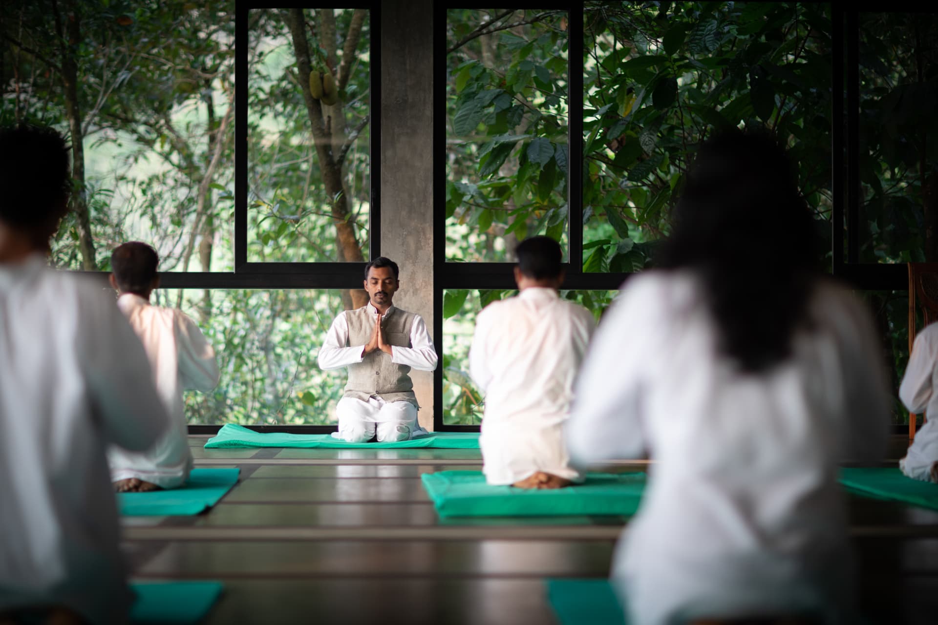 Guests seated in meditation with their teacher in the forest-facing yoga hall at Prakriti Shakti