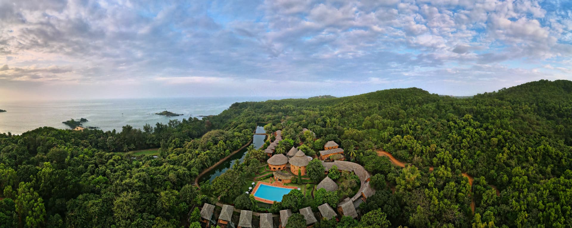 Aerial view of SwaSwara Gokarna CGH Earth — thatched laterite villas, pool and lake set within forest above the Arabian Sea