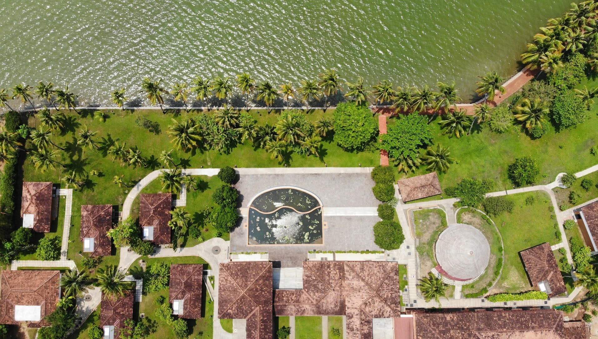 Aerial view of Kalari Rasayana Paravur Kerala CGH Earth — tiled cottages, lily pond and coconut palms beside the backwaters