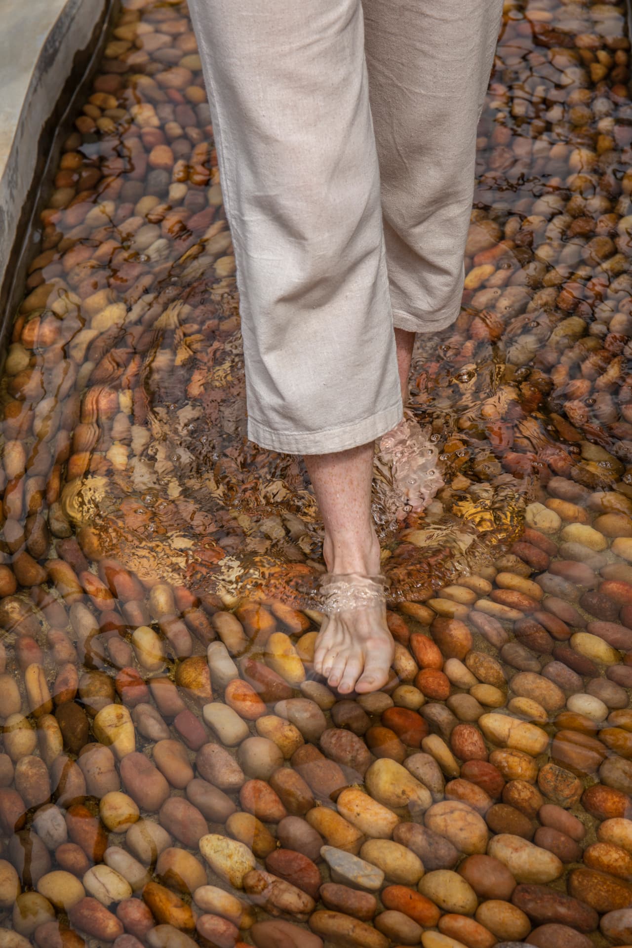 Bare feet walking through shallow water over smooth river pebbles on the reflexology walk