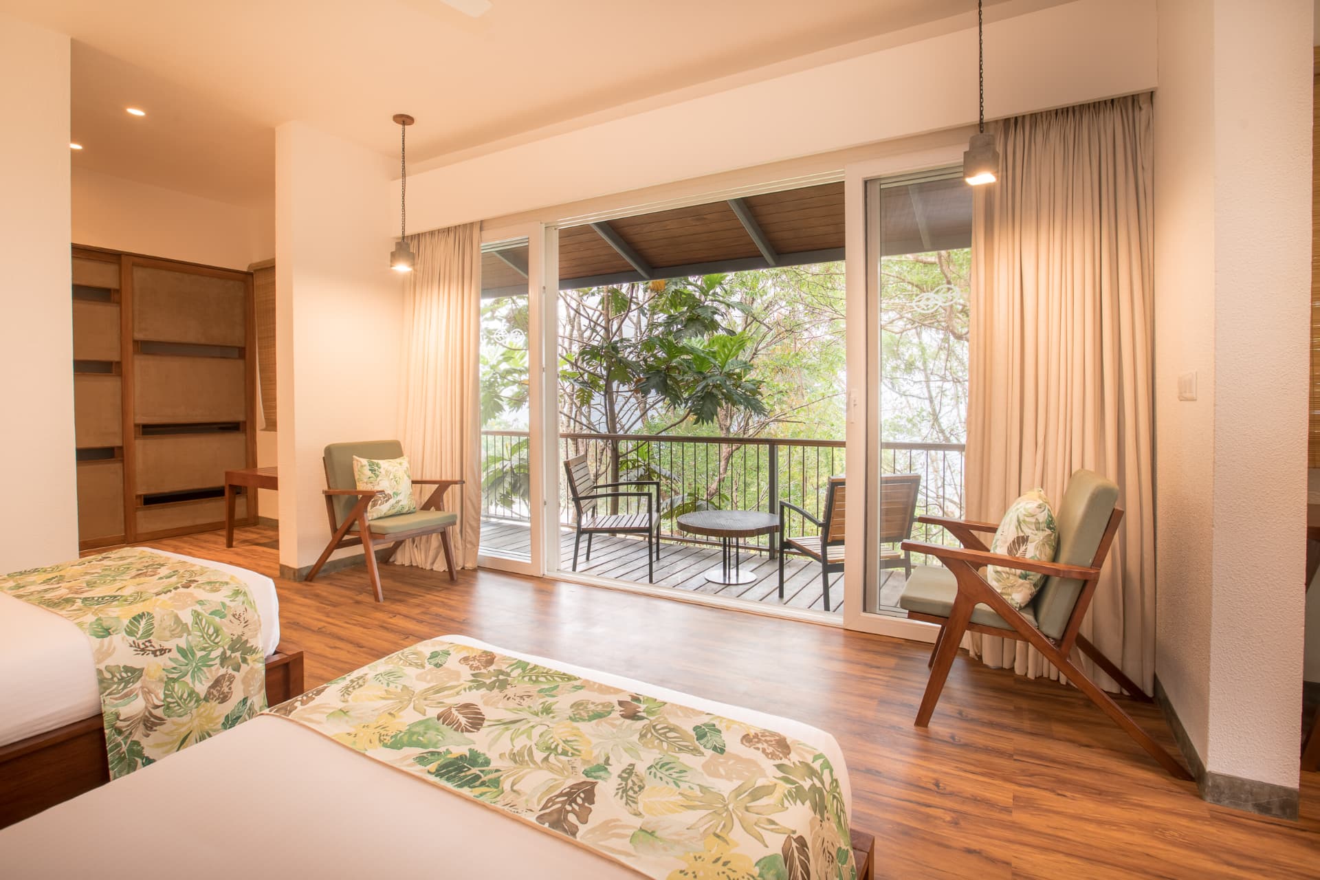 Twin room with wooden floors, cane chairs and a shaded balcony overlooking the treetops at Prakriti Shakti
