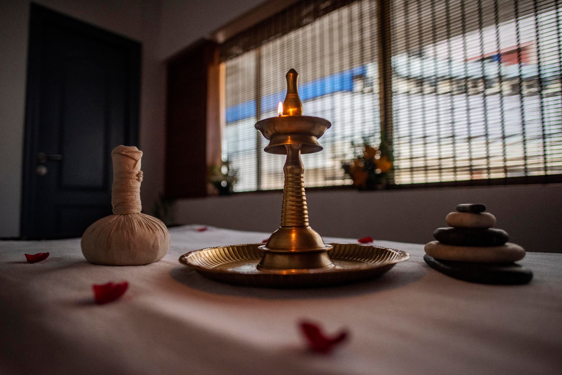 Ayurveda spa setting with brass oil lamp, hot stones and herbal compresses