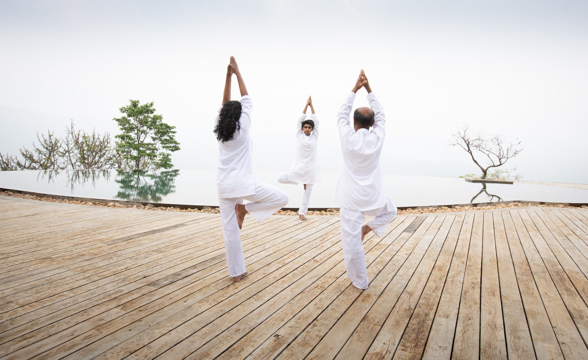 Three guests in tree pose on the timber deck beside the infinity pool at Prakriti Shakti