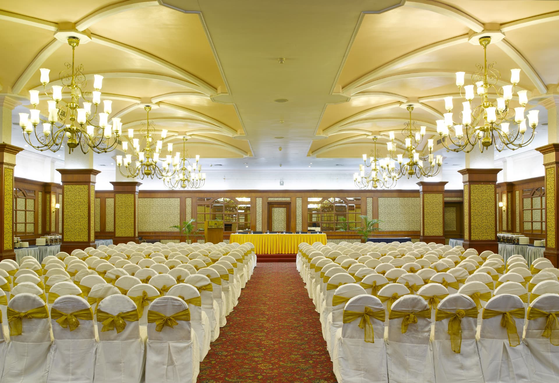 Grand banquet hall set with rows of white chairs and chandeliers