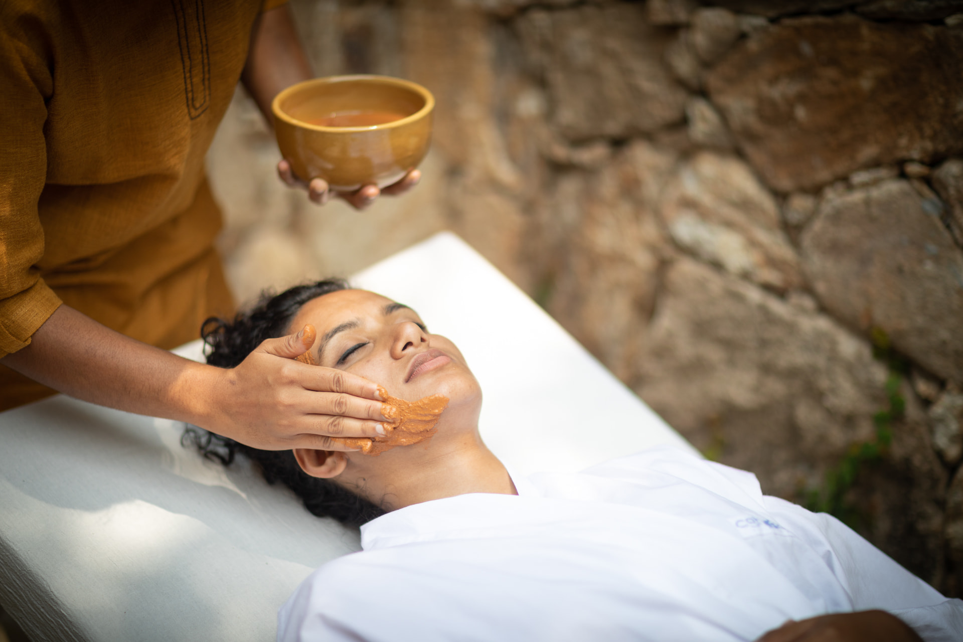 Therapist applying a herbal clay face pack during a naturopathy treatment at Prakriti Shakti