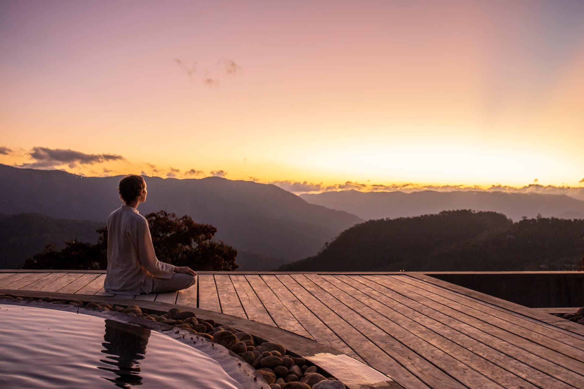 Guest seated in meditation on the timber deck above the valley at dusk, Prakriti Shakti Kerala