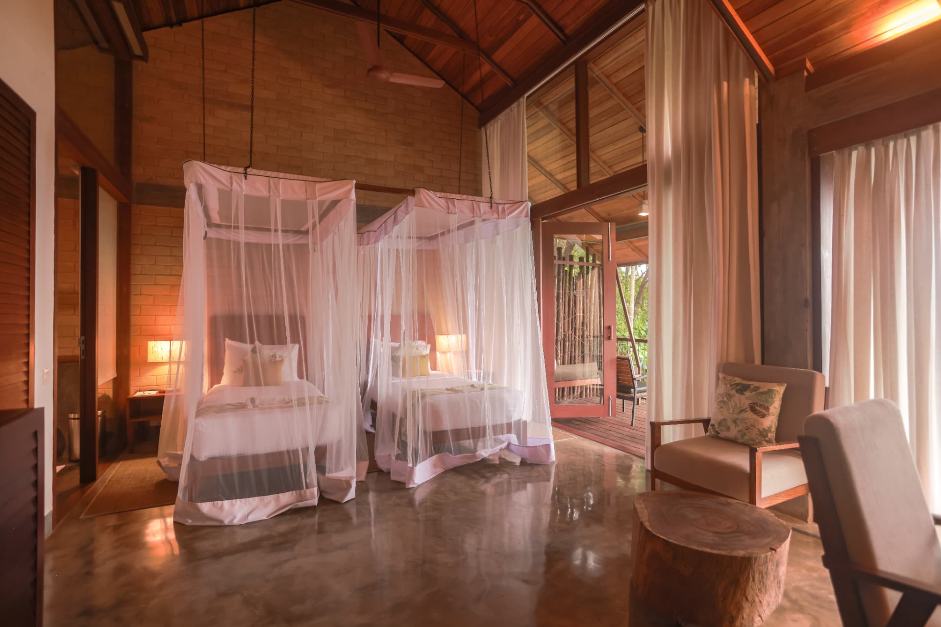 Two canopied beds with mosquito nets in a brick and timber villa at Prakriti Shakti, Kerala