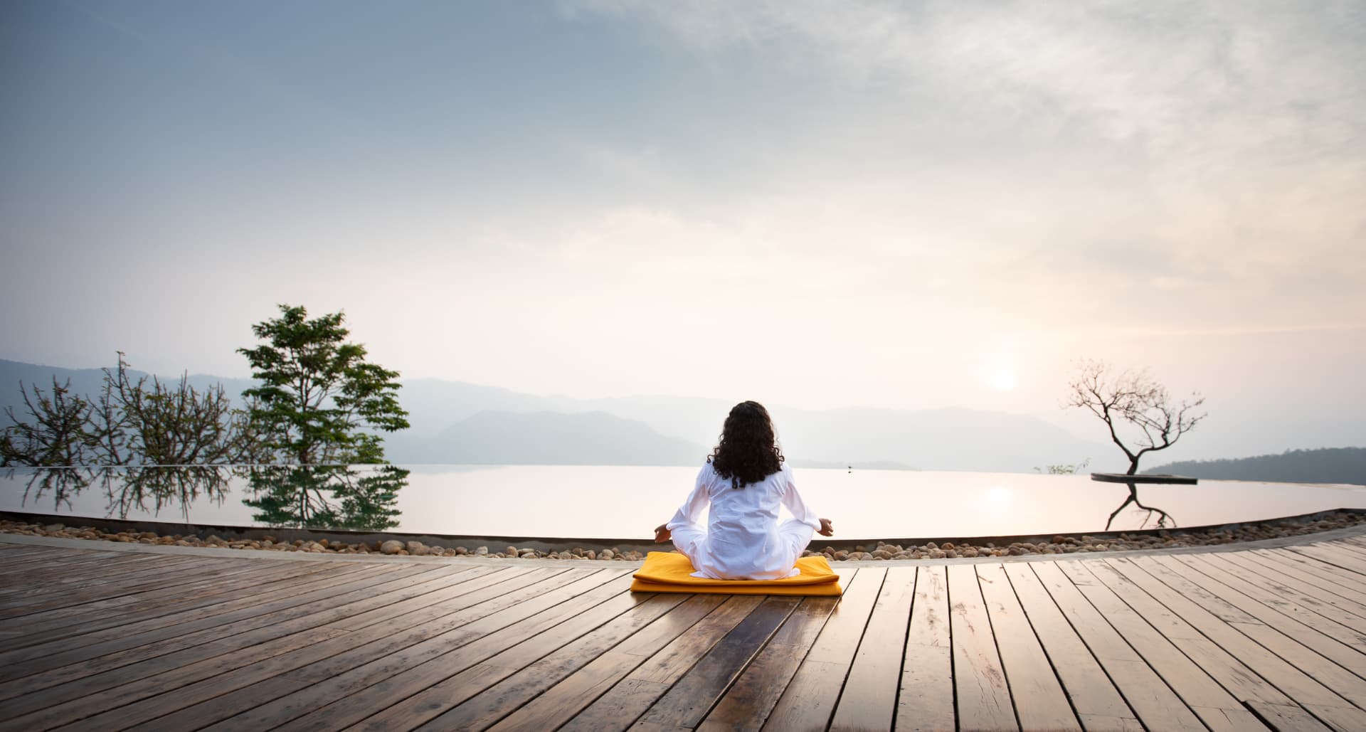 Guest meditating alone on the deck at sunrise above the still infinity pool, Prakriti Shakti Kerala