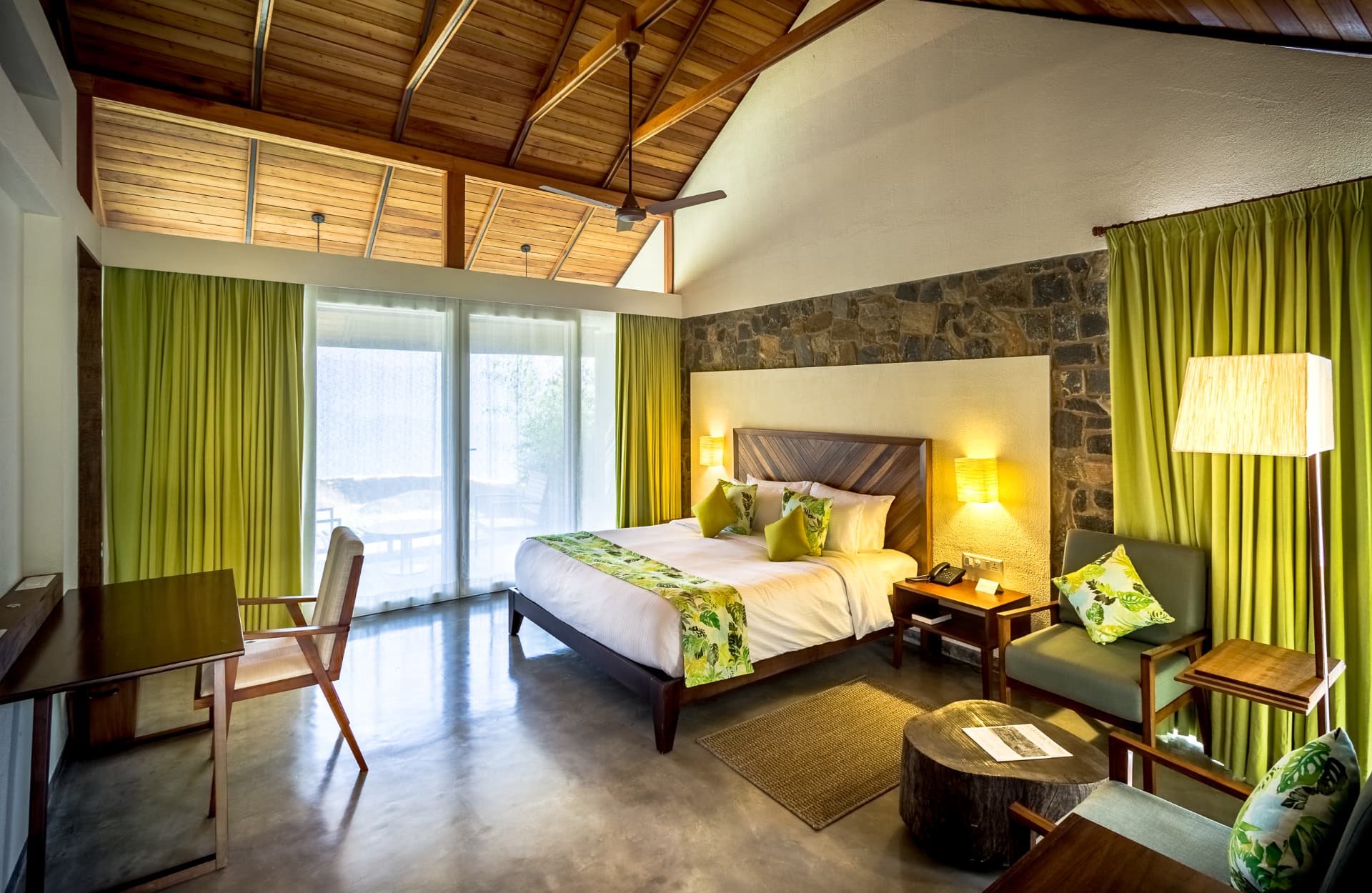 Garden-view room at Prakriti Shakti with timber ceiling, stone wall and green drapes opening to a private deck
