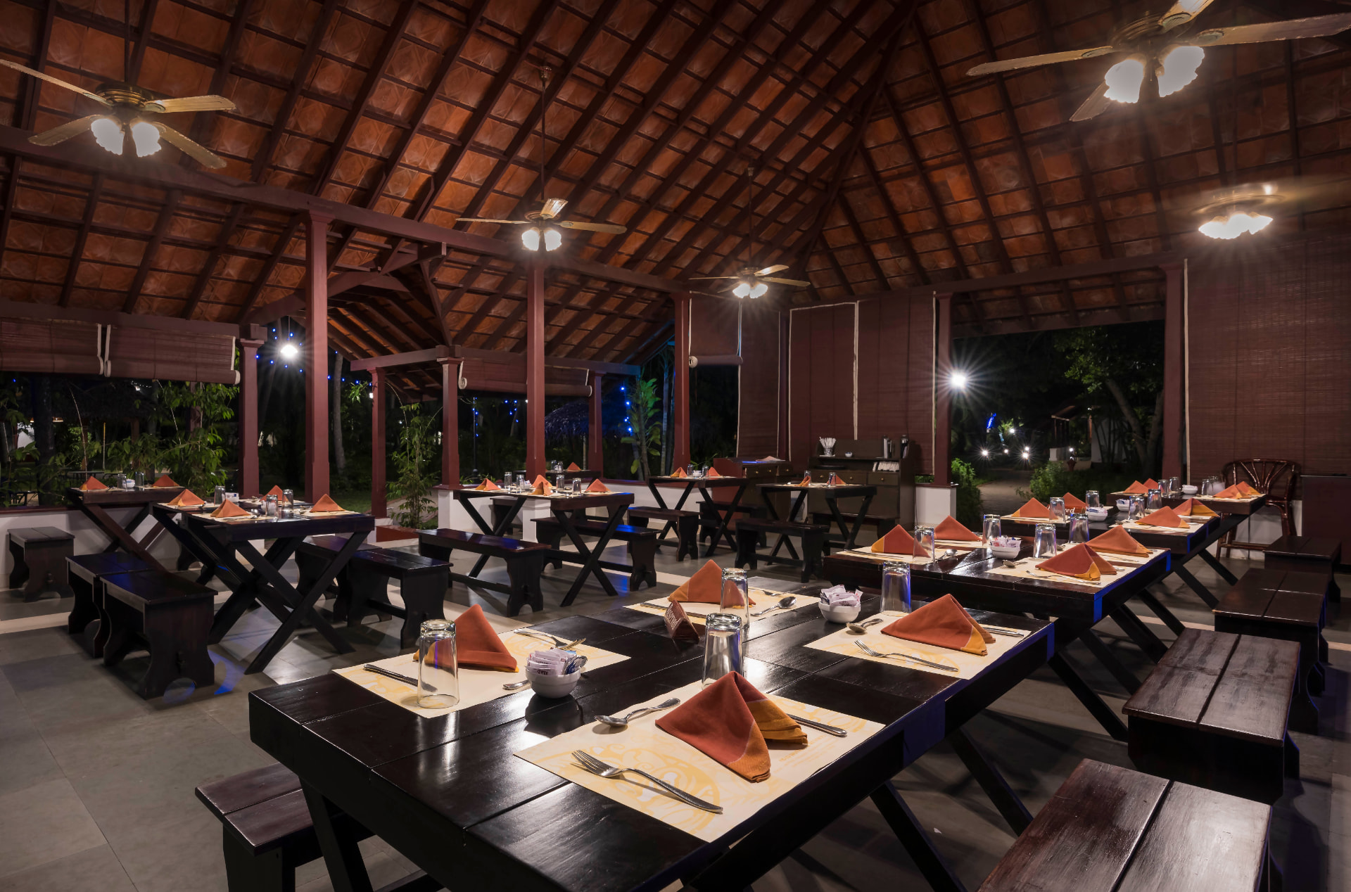 Open-sided beachside restaurant with timber tables under a tiled Kerala roof